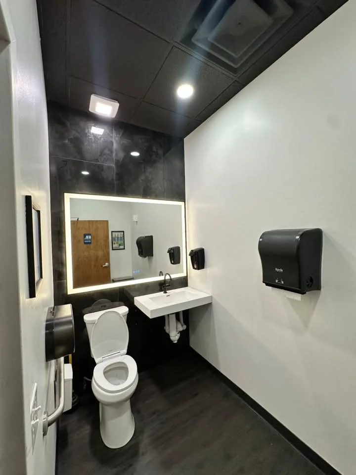 Completed commercial bathroom renovation with backlit mirror and tile accent wall